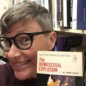 a picture of The ArQuives volunteer Kate Zieman holding up a book titled “The Homosexual Explosion”, by Norm Winski.