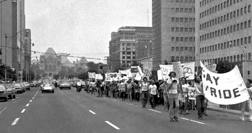 a photograph from the 1972 march on University Avenue in Toronto, Ontario, with individuals holding signs and speaking into loudspeakers. Photograph taken by Jearld Moldenhauer, http://www.jearldmoldenhauer.com