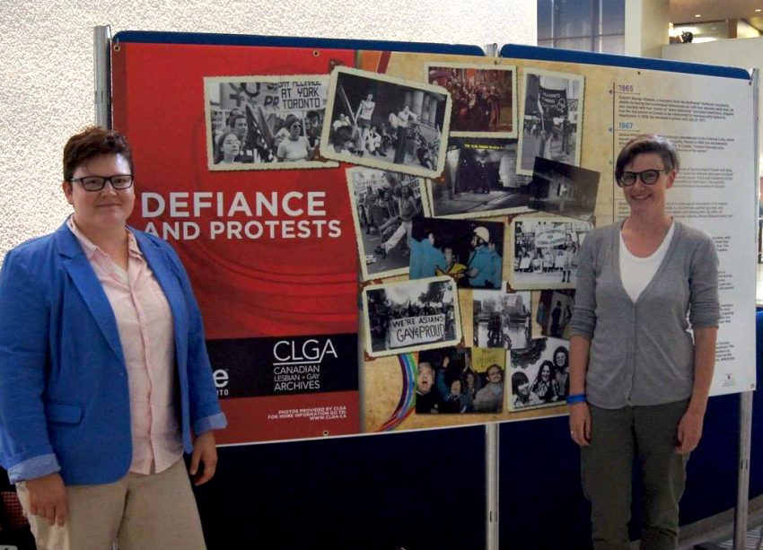 Rebecka Sheffield and Kate Zieman in front of display panel featuring LGBTQ2+ "Defiance and Protests" stories.