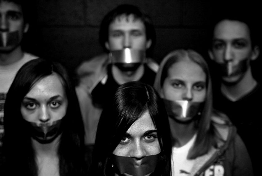 image description: black and white head shot photograph of a group of students with metallic tape across their mouths in support of A Day of Silence. Credit: "Day of Silence" by Gitgat is licensed under Creative Commons BY-NC-ND 2.0
