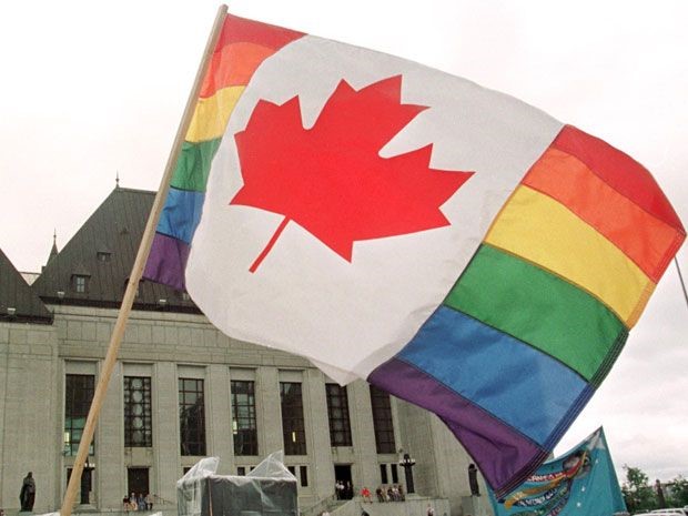 a photograph of a Pride Flag with the Canadian Maple Leaf in the middle waving in the air in front of The Supreme Court of Canada building.