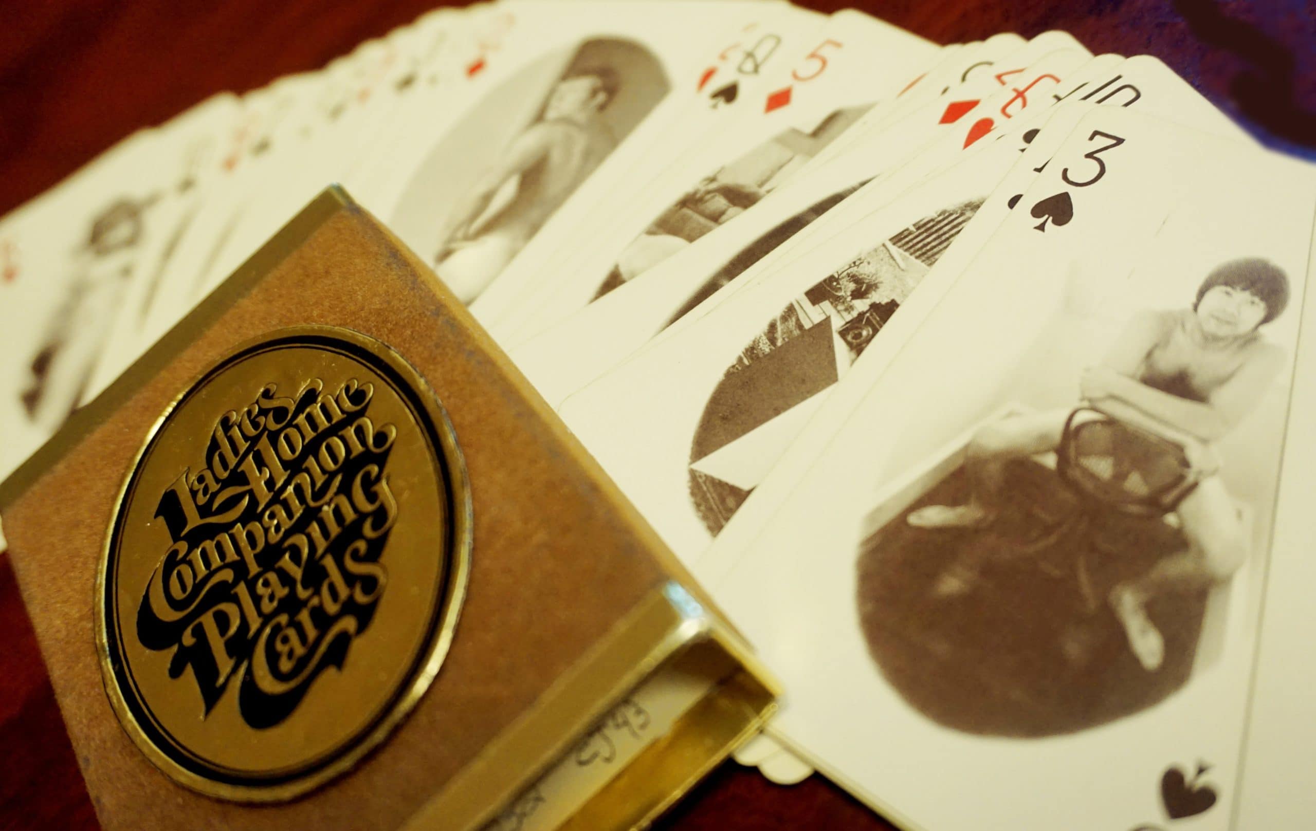 Ladies Home Companion playing cards spread out on a table. The card case is in the foreground and the 3 of spades remains in focus with an Asian nude model on it.