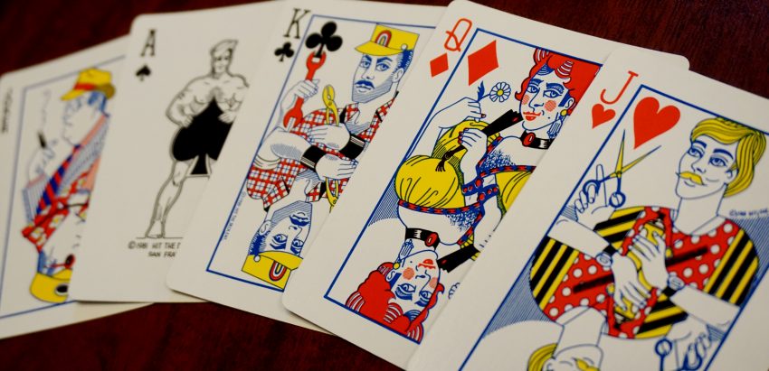 Five illustrated playing cards (Joker, Ace, King, queen, and Jack) decorated with queer imagery, including a muscular sailor, construction worker, drag queen, and hairstylist.