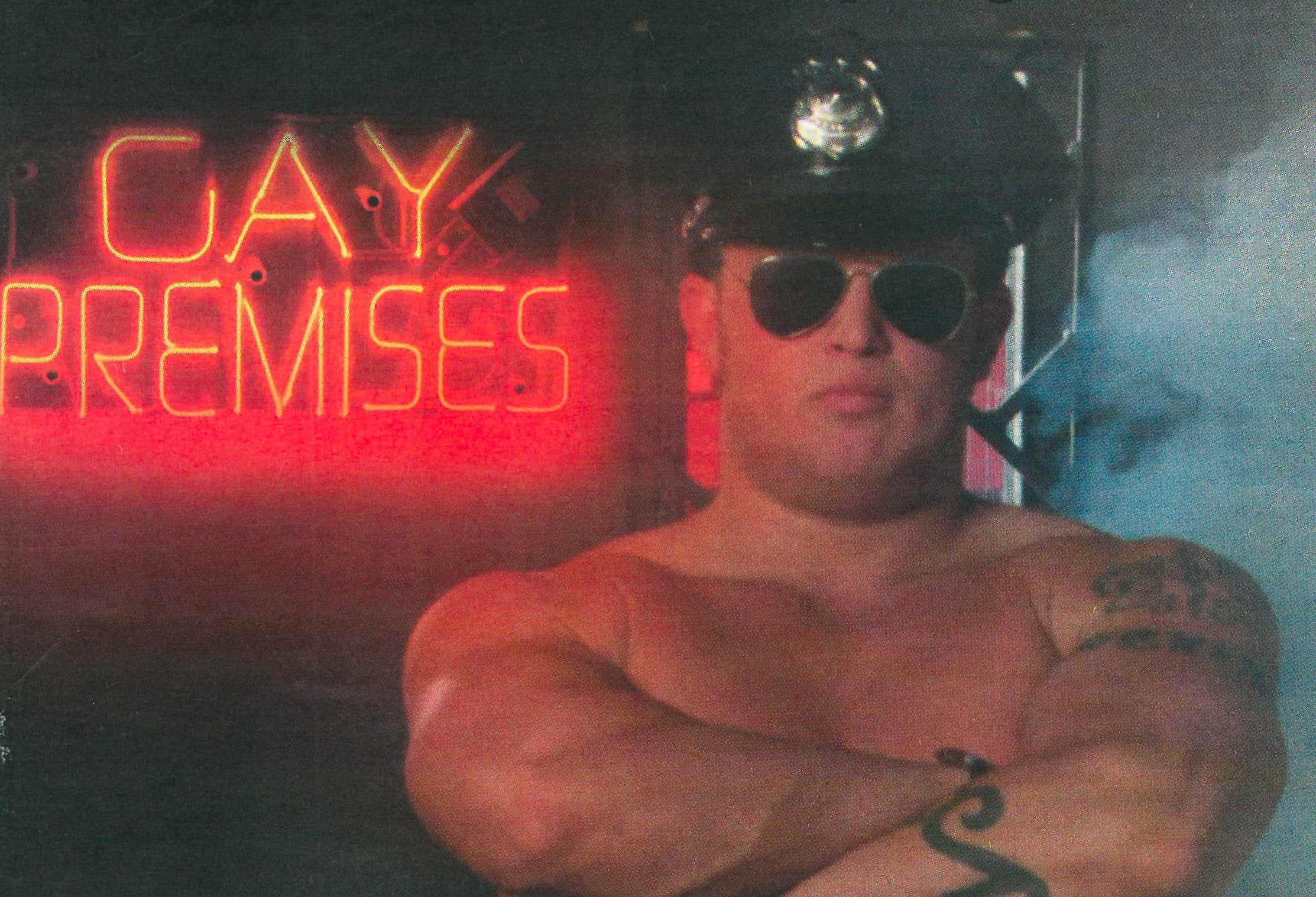 An image from the January 2003 issue of Outlooks magazine featuring a shirtless man wearing an officer's cap in front of the Goliath's Saunatel "Gay Premises" sign.