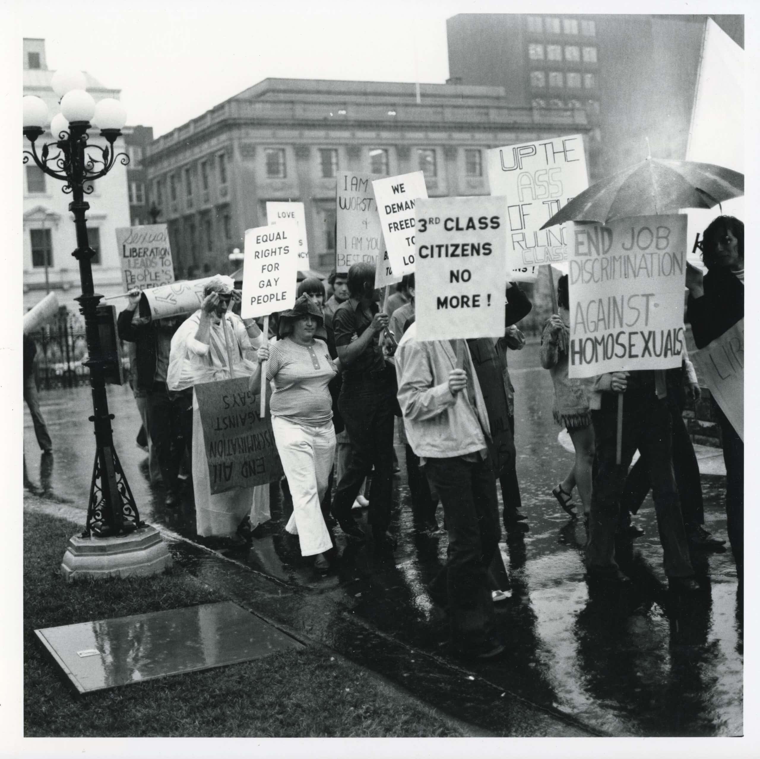Demonstrators hold signs with text including: “3rd class citizens no more!” and “End job discrimination against homosexuals.”