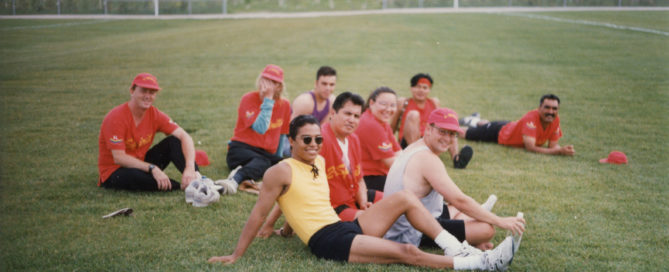 9 people lounge on the grass smiling, most in red jerseys