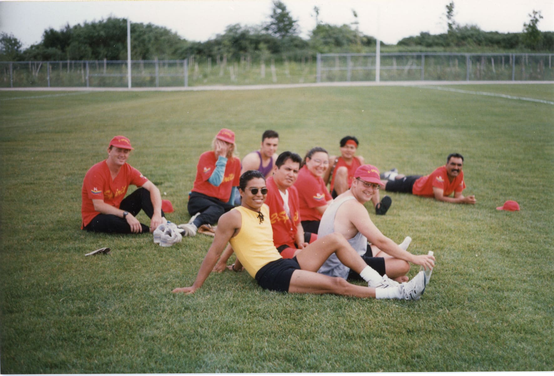 9 people lounge on the grass smiling, most in red jerseys