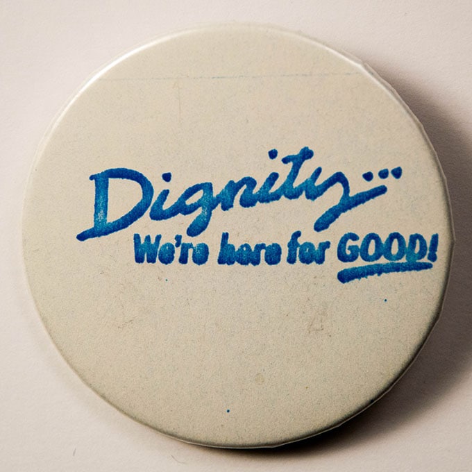 White button with blue text reading “Dignity: We’re here for GOOD!”