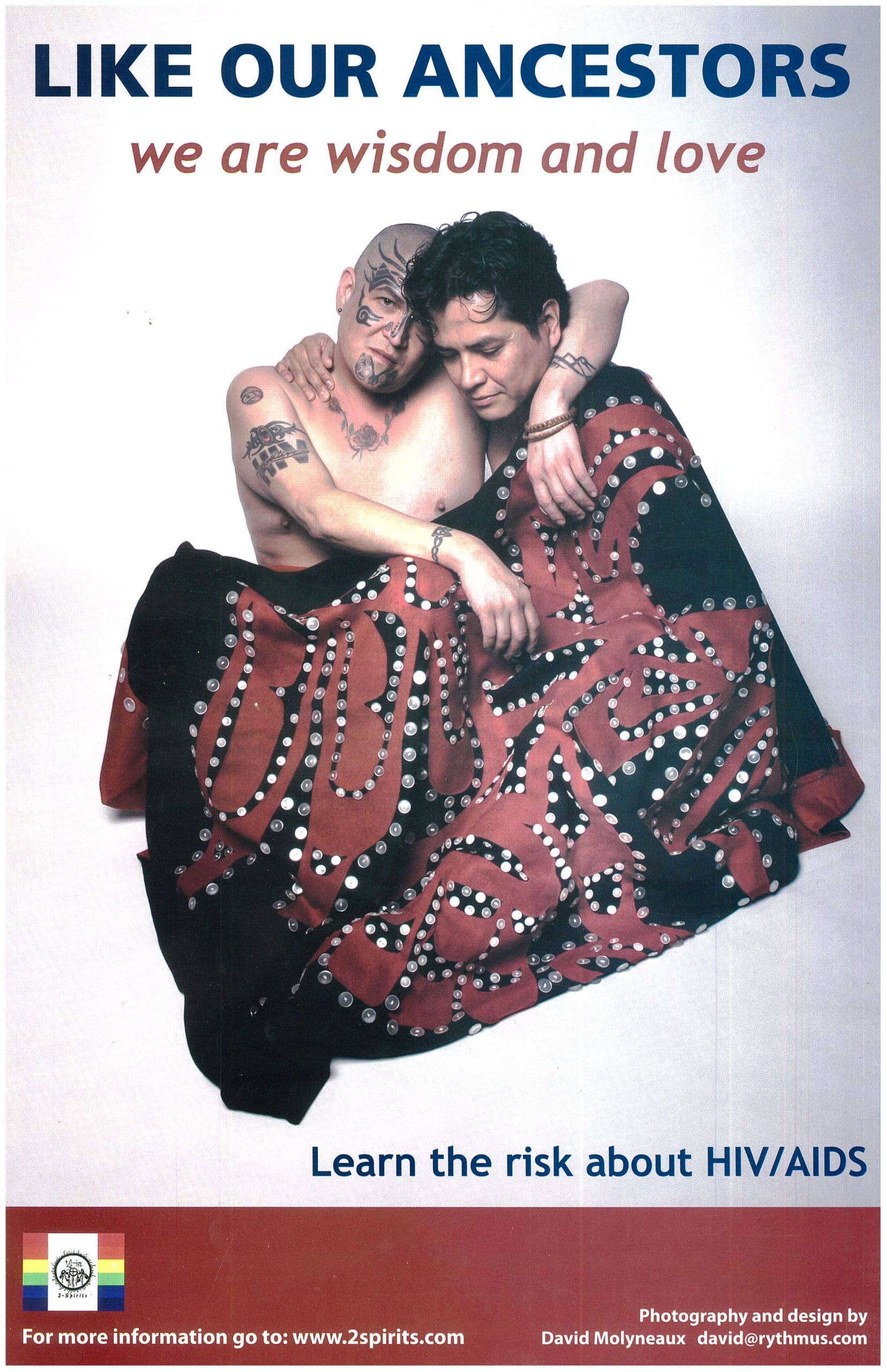 A person with a shaved head and tattoos and a person with wavy dark hair are embracing one another. Their bodies are partially covered with a black and red button blanket. Text at the top reads, “like our ancestors we are wisdom and love.” Text at the bottom reads, “learn the risk about HIV/AIDS.” In the bottom left corner, there is an image of a Pride flag with a Two-Spirit symbol in the centre.