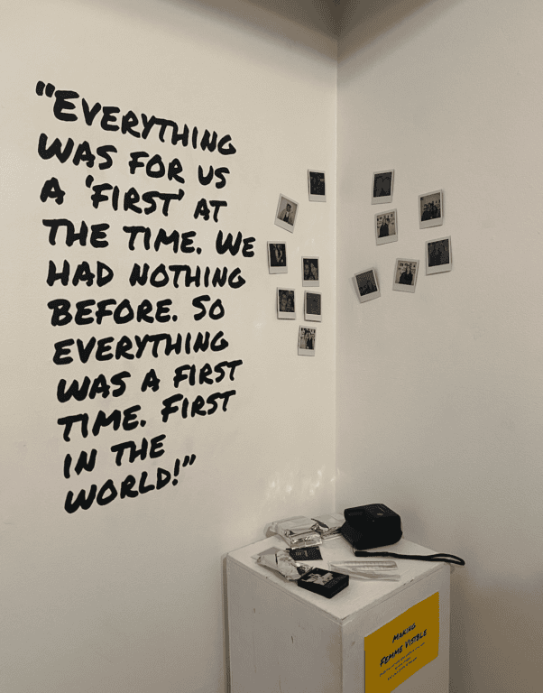 A white wall featuring several polaroid photographs. Black paint reads "Everything was for us a 'first' at the time. We had nothing before. So everything was a first time. First in the world!"
